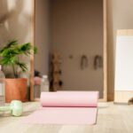 Minimalist home workout scene with a rolled yoga mat, light green dumbbell, and water bottle in soft natural light beside indoor plants.