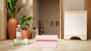 Minimalist home workout scene with a rolled yoga mat, light green dumbbell, and water bottle in soft natural light beside indoor plants.