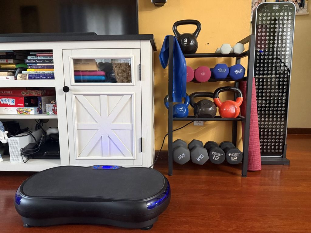 Home gym with dumbbells, kettlebells, resistance bands, red light therapy, and a vibration therapy platform