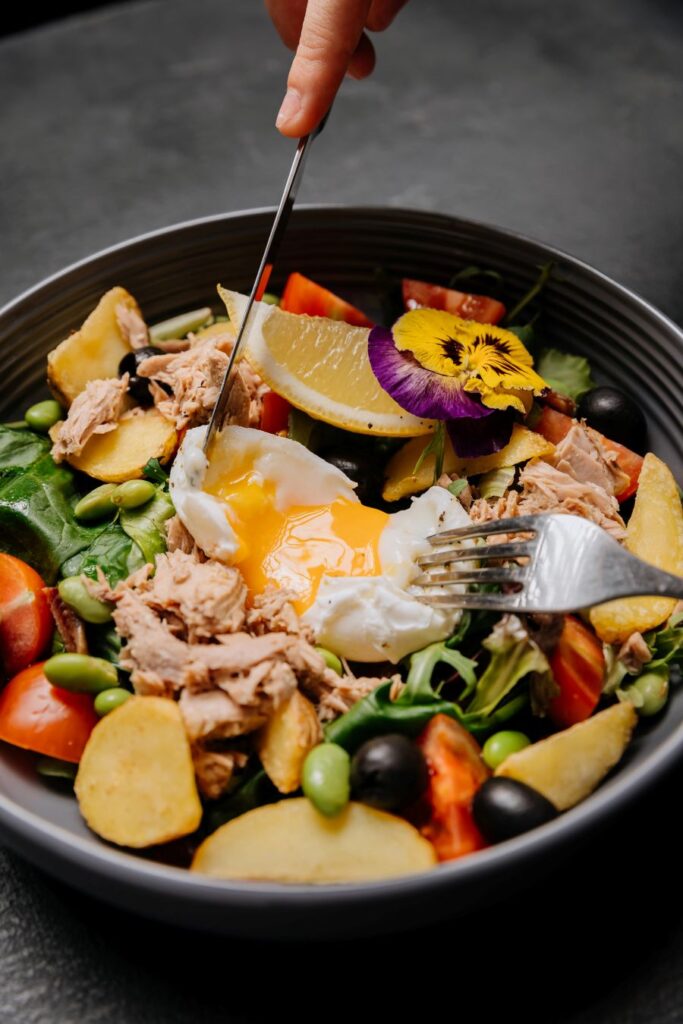 Colorful tuna salad bowl with greens, vegetables, roasted potatoes, and a poached egg.