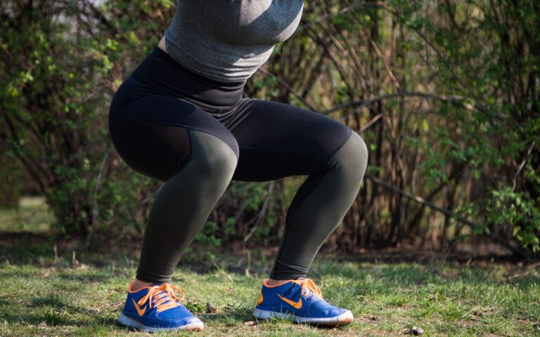Person practicing a grounding squat outdoors on grass with trees in the background