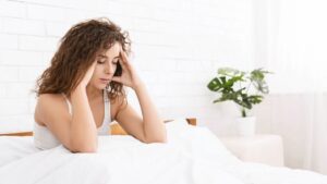 woman sitting in bed with hands on temples feeling wired tired and numb from stress