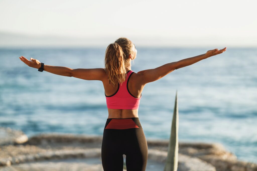 Person opening their arms toward the ocean, practicing somatic movement to support mind‑body connection and nervous system regulation.