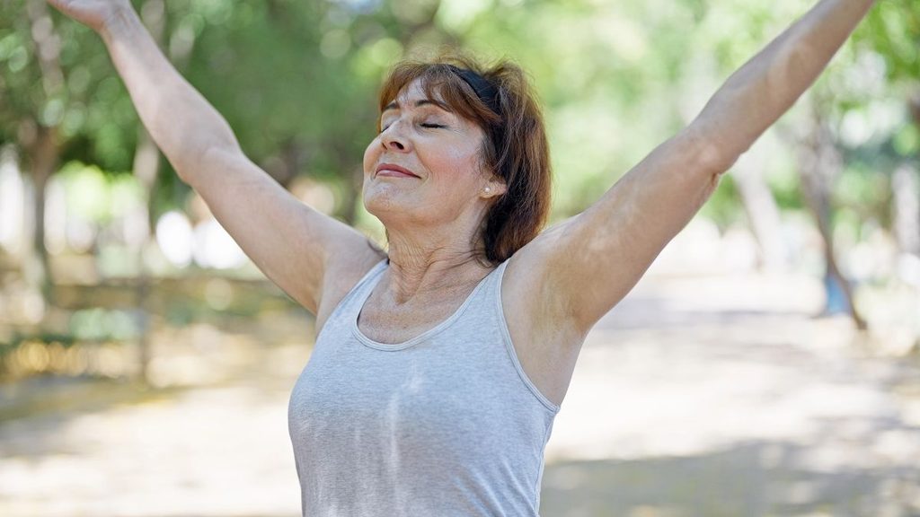 Woman with arms raised outdoors, embodying confidence and relief after overcoming kinesiophobia